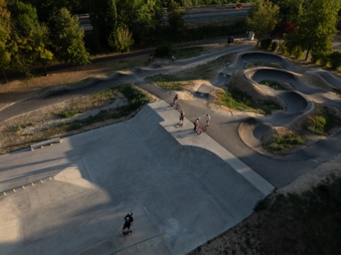 Luftaufnahme des Skateparks am Schwarzen Platz mit Personen an der Kante zum Pumptrack und einem fahrenden Skateboarder.