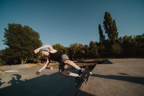 Person springt mit Skateboard über die Kante einer Betonrampe in einem Skatepark bei Abendlicht.