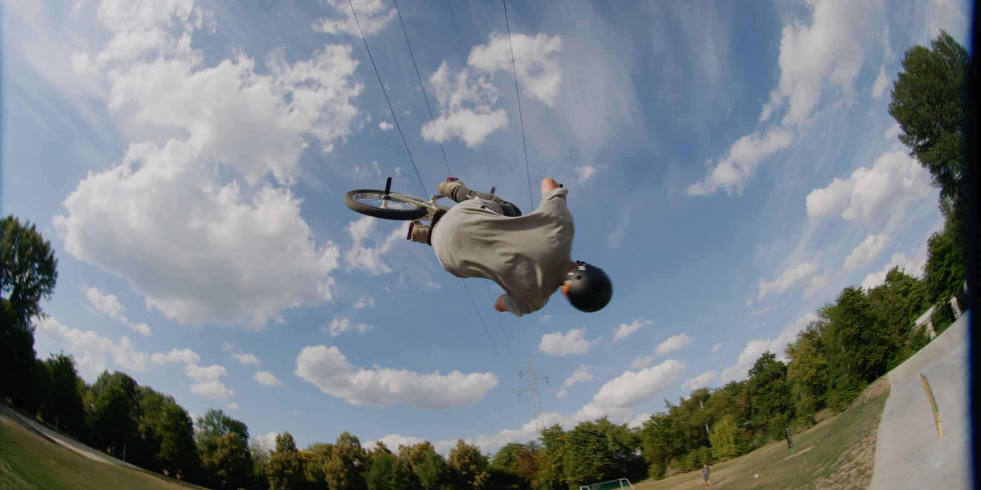 BMX-Fahrer kopfüber in der Luft über dem Skatepark Krems, dahinter Wolkenhimmel