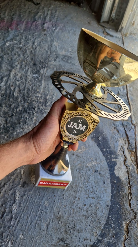 Goldener Pokal mit JAM-Medaillon, in einer Hand gehalten